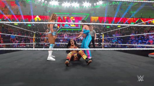 You call your partner into the ring and stand next to your opponent as she sits on the mat. In tandem, you and your partner both swing your hips into her face at the same time, squeezing your opponents head into a vice grip!
