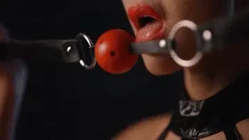 Le pones una mordaza de bola, así que ahora todo lo que puede hacer es gemir y babear goteando sobre sus tetas.